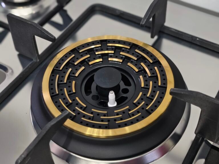 Close-up of the GCS-73301-B-04 gas hob: a built-in burner with a round brass and black design, featuring detailed holes and geometric patterns, surrounded by four sturdy black pan supports. Perfect for 3 burner setups with elegant brass burners.