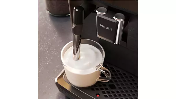 The vrs_2200-05.webp coffee machine froths milk in a clear glass cup with its steam wand, creating rich froth while the cup rests on the drip tray.