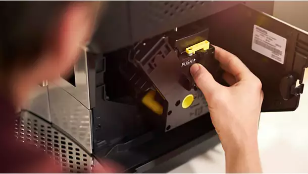 A hand removes or inserts a yellow and black component labelled PUSH from the open side panel of the Philips vrs_2200-08.webp coffee machine.