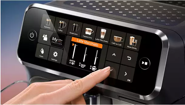 A close-up of a person’s hand pressing the touchscreen on the vrs_5400-07-ac.webp coffee machine, selecting "Latte Macchiato" from various coffee options displayed.